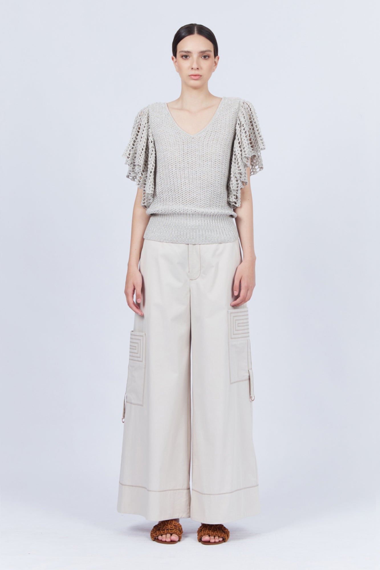 A woman modeling Belén palazzo pants in pristine white color, featuring side patch pockets with metal buckle straps.