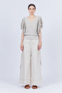A woman modeling Belén palazzo pants in pristine white color, featuring side patch pockets with metal buckle straps.