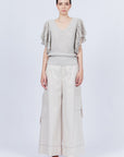 A woman modeling Belén palazzo pants in pristine white color, featuring side patch pockets with metal buckle straps.