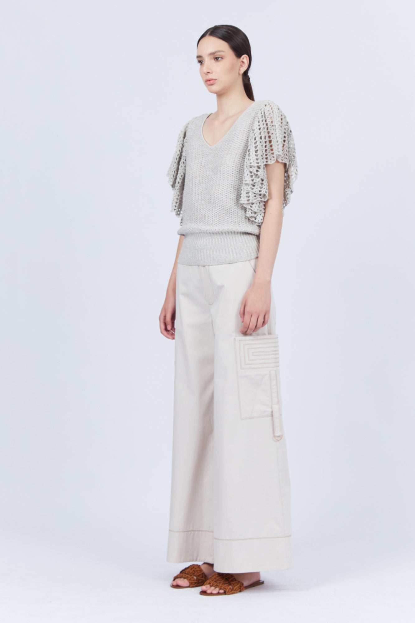 A woman modeling Belén palazzo pants in pristine white color, featuring side patch pockets with metal buckle straps.