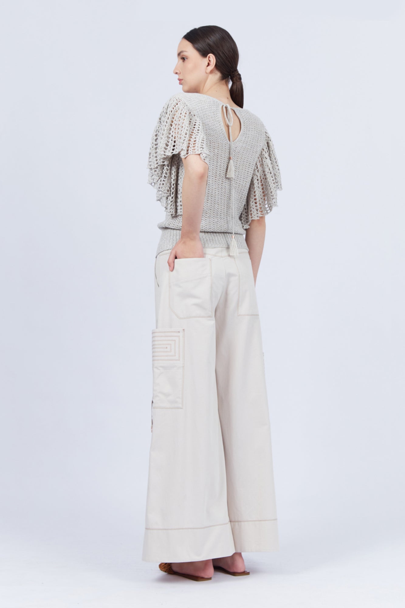 A woman modeling Belén palazzo pants in pristine white color, featuring side patch pockets with metal buckle straps.