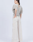 A woman modeling Belén palazzo pants in pristine white color, featuring side patch pockets with metal buckle straps.