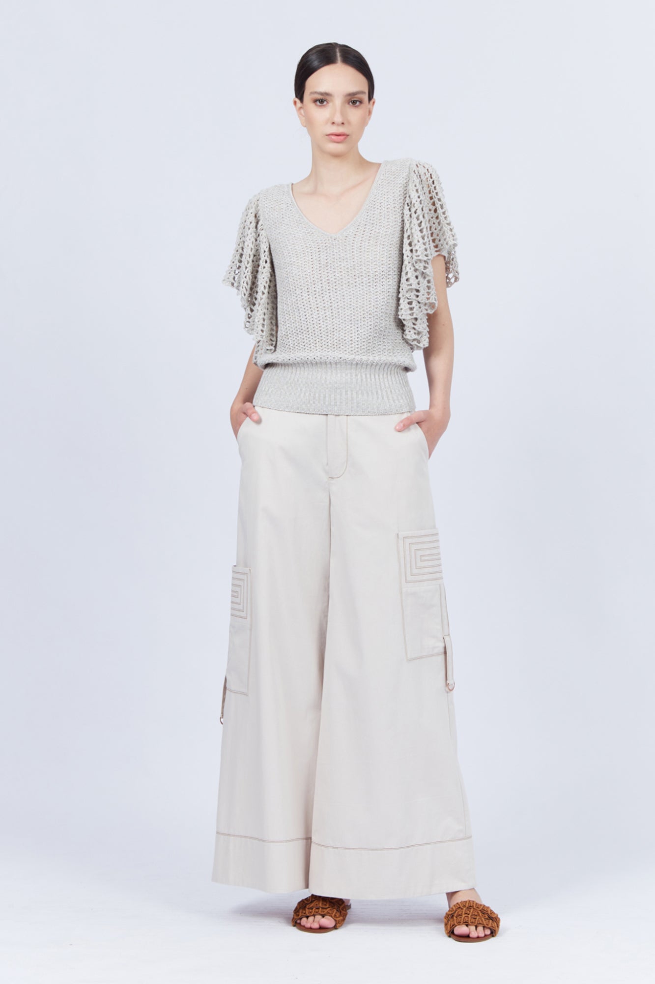 A woman modeling Belén palazzo pants in pristine white color, featuring side patch pockets with metal buckle straps.