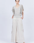 A woman modeling Belén palazzo pants in pristine white color, featuring side patch pockets with metal buckle straps.