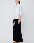 Side view of the white Hebe Blouse, showcasing the elegant, sculptural drape of the hem.