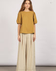 A model wearing an olive green Jamie Top with a round neckline and ¾ sleeves, paired with light-colored wide-leg pants.