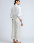 Woman wearing a white blouse and light-colored pants on a plain background