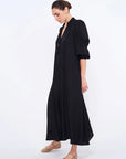 Side profile of the black Carlie Dress, highlighting the draped, asymmetrical skirt.