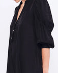 Side profile of the black Carlie Dress, highlighting the draped, asymmetrical skirt.