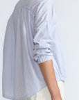 Hebe Blouse in Light Blue Stripes – Relaxed blouse with lapel collar, hidden buttons, asymmetrical hem, and elasticized long sleeves.