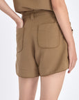 Lira Short in Taupe – Chic mid-rise linen shorts with elasticated waistband, metal-tipped belt, and patch pocket detailing.