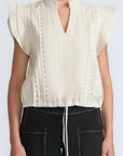 Pria Blouse in Prestine – Elegant sleeveless blouse in pima cotton with tonal V-neck, Greca trim, ruffle detail, and hem with pullers.