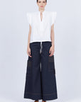Pria Blouse in White – Sleeveless pima cotton blouse with V-neckline, Greca trim, tonal stitching, ruffle sleeves, and hem pullers.