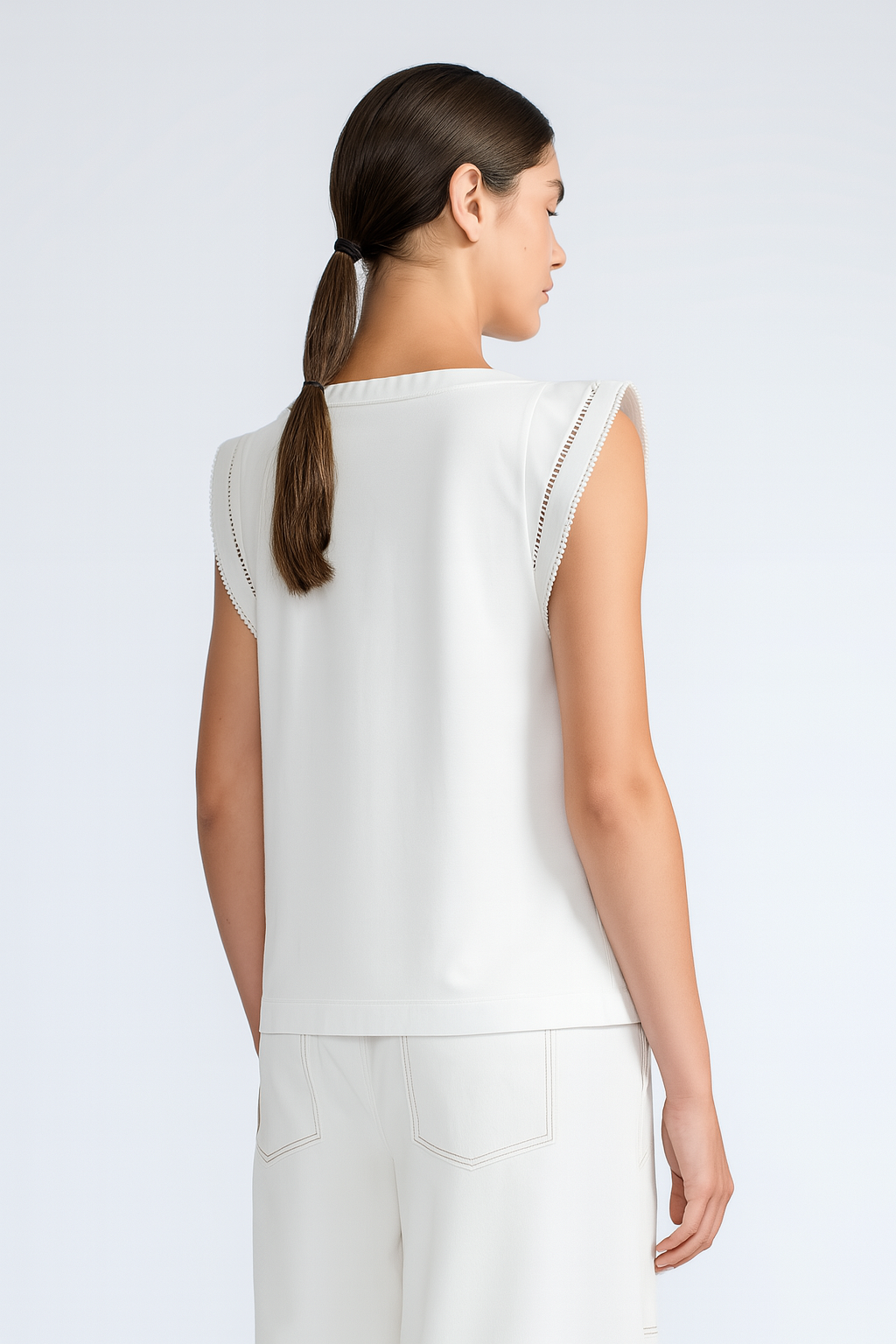 Woman wearing a white sleeveless top and pants on a plain background