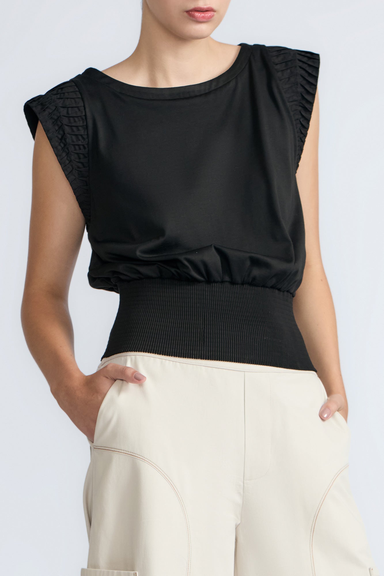 Black sleeveless top with textured shoulders worn by a person on a light gray background