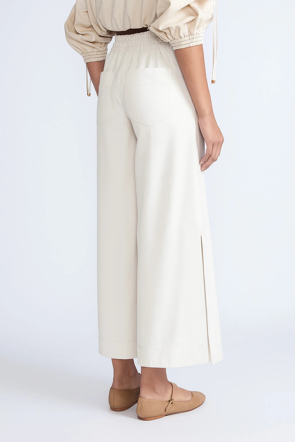 Person wearing a beige blouse and white pants on a light gray background