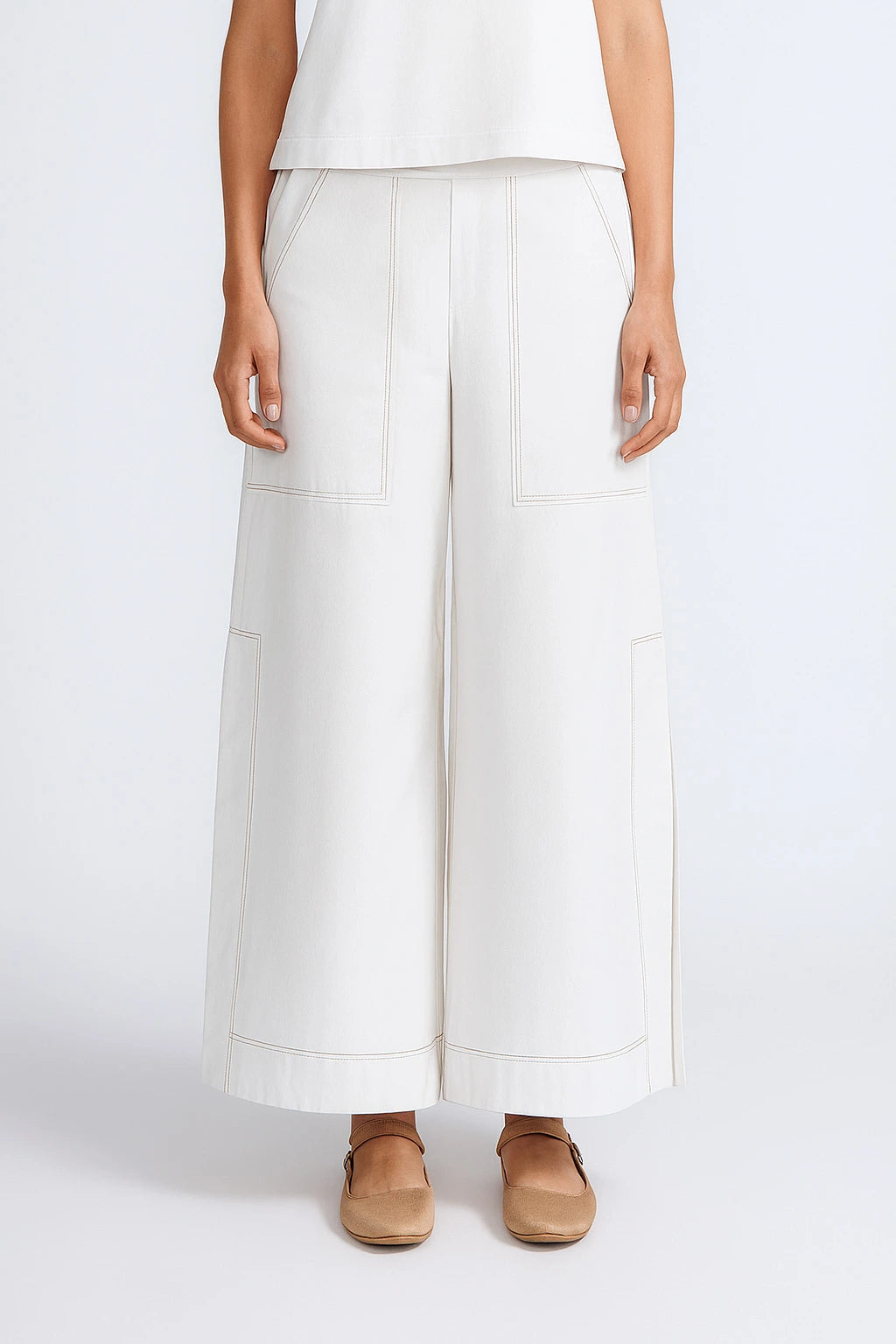Person wearing white wide-leg pants and brown shoes on a white background