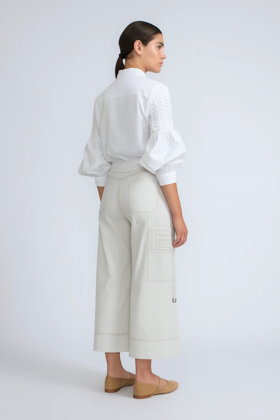 Woman wearing a white blouse and light-colored pants on a plain background