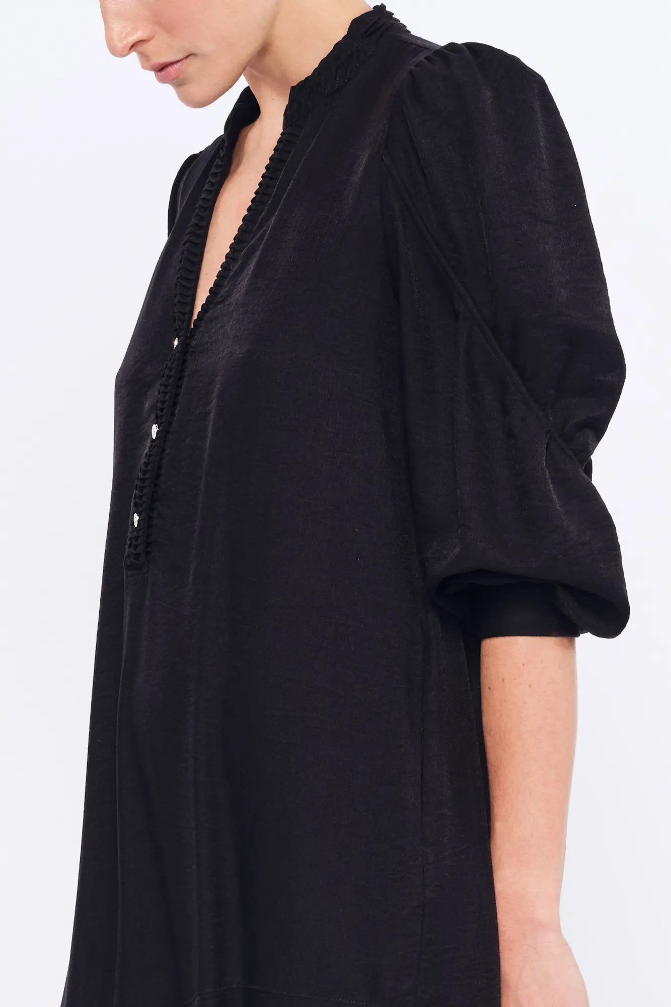 Side profile of the black Carlie Dress, highlighting the draped, asymmetrical skirt.