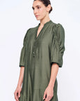 Side view of the Olive Carlie Dress, showcasing the elegant movement of its asymmetrical hem.
