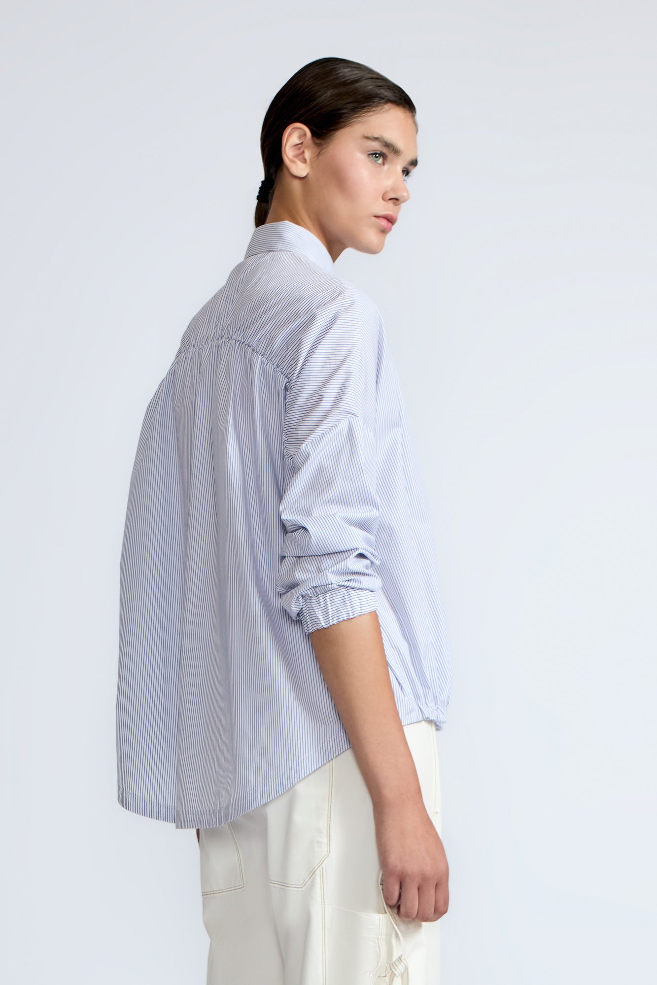 Hebe Blouse in Light Blue Stripes – Relaxed blouse with lapel collar, hidden buttons, asymmetrical hem, and elasticized long sleeves.