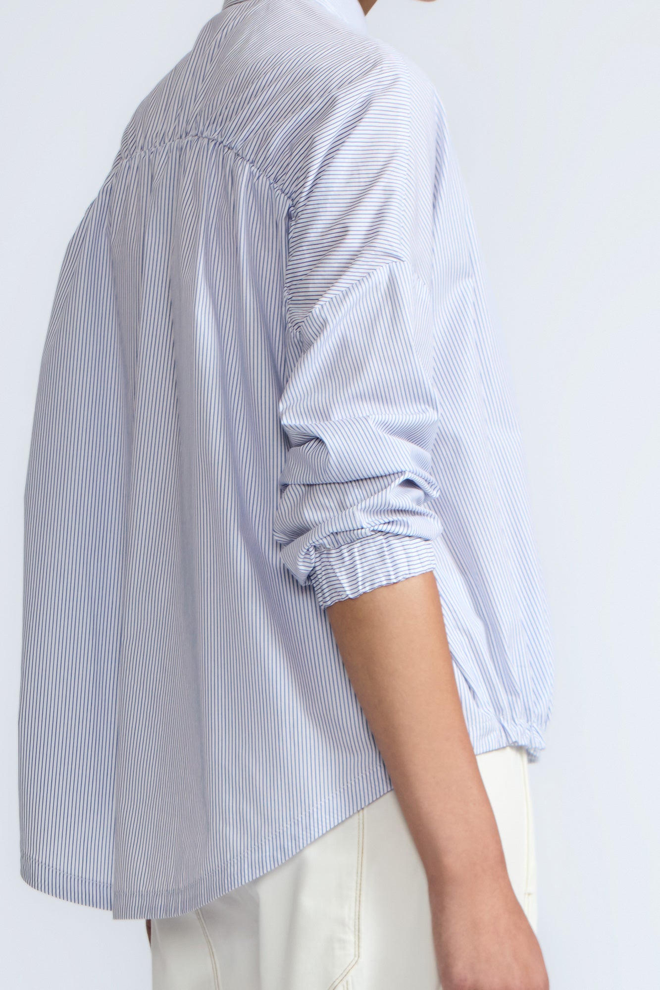 Hebe Blouse in Light Blue Stripes – Relaxed blouse with lapel collar, hidden buttons, asymmetrical hem, and elasticized long sleeves.