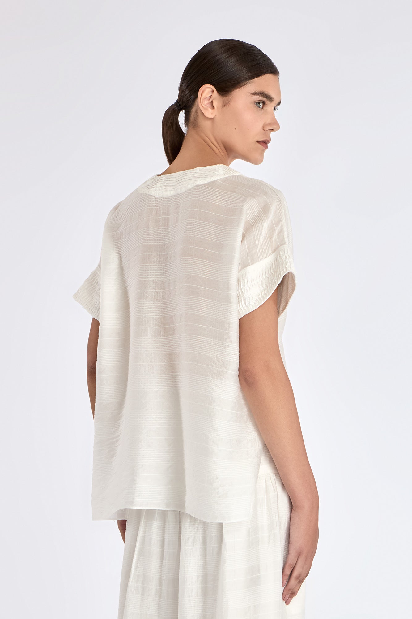 Ivy Blouse in Off White – V-neck short sleeve blouse with tonal hem detail and relaxed silhouette in rayon and nylon blend.
