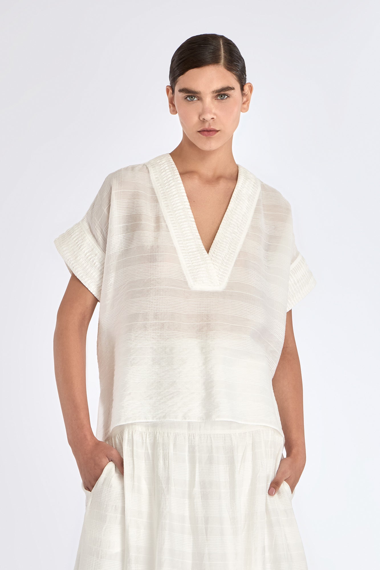 Ivy Blouse in Off White – V-neck short sleeve blouse with tonal hem detail and relaxed silhouette in rayon and nylon blend.