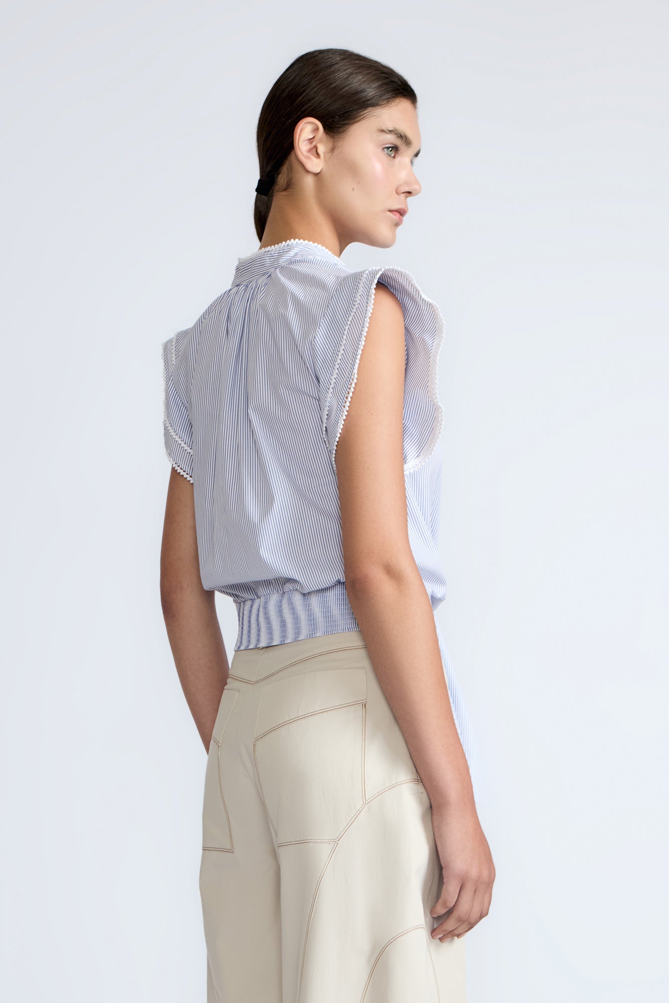 Oriana Blouse in Light Blue Stripes – Cotton blouse with V-neck, Neru collar, ruffled sleeves, appliqué trim, and tie-front hem.