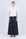 Pria Blouse in White – Sleeveless pima cotton blouse with V-neckline, Greca trim, tonal stitching, ruffle sleeves, and hem pullers.