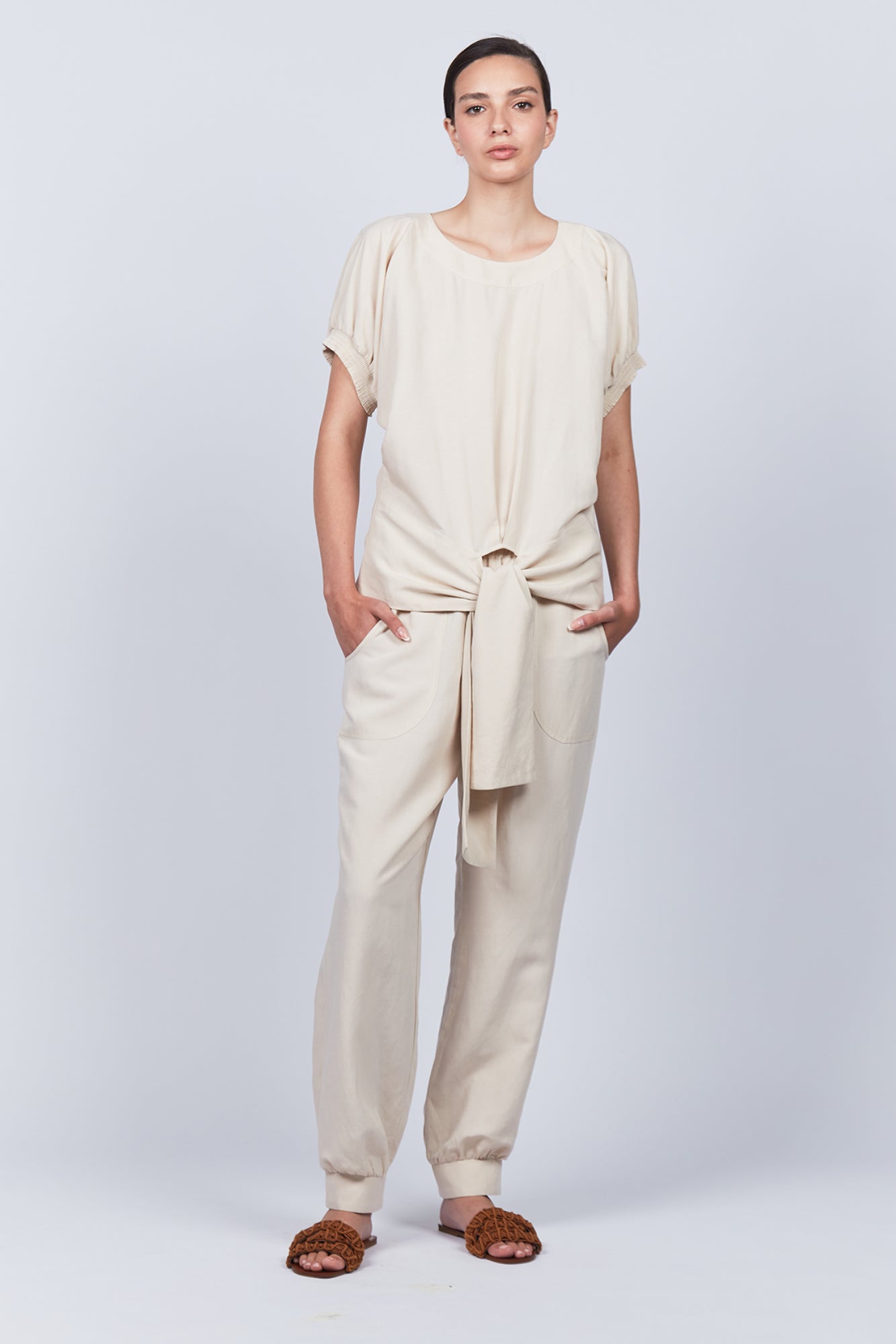 Shelby Blouse in Ecru with a round neck, button-back detail, elasticated short sleeves, and adjustable tie hem.