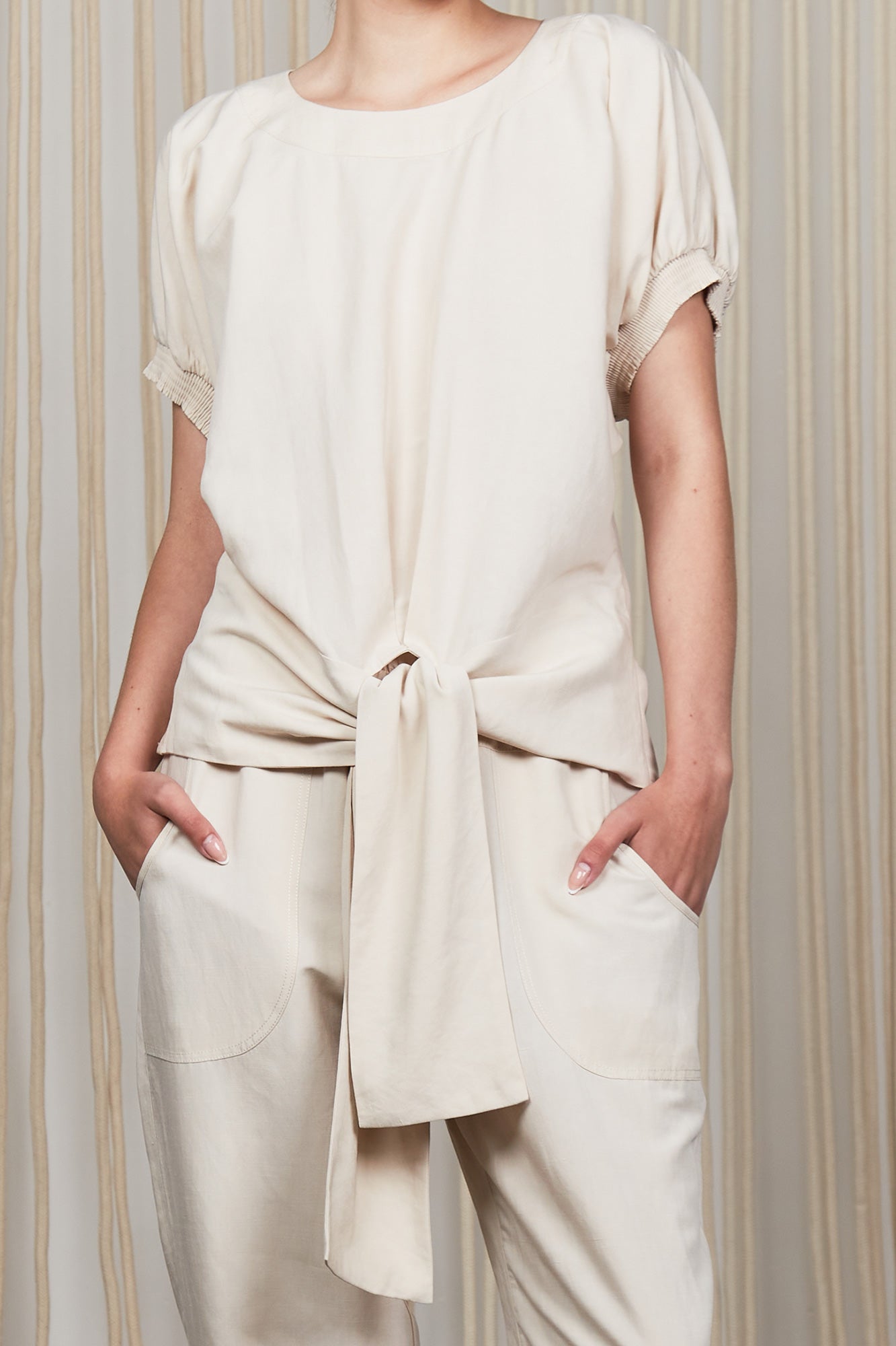 Shelby Blouse in Ecru with a round neck, button-back detail, elasticated short sleeves, and adjustable tie hem.