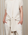 Shelby Blouse in Ecru with a round neck, button-back detail, elasticated short sleeves, and adjustable tie hem.