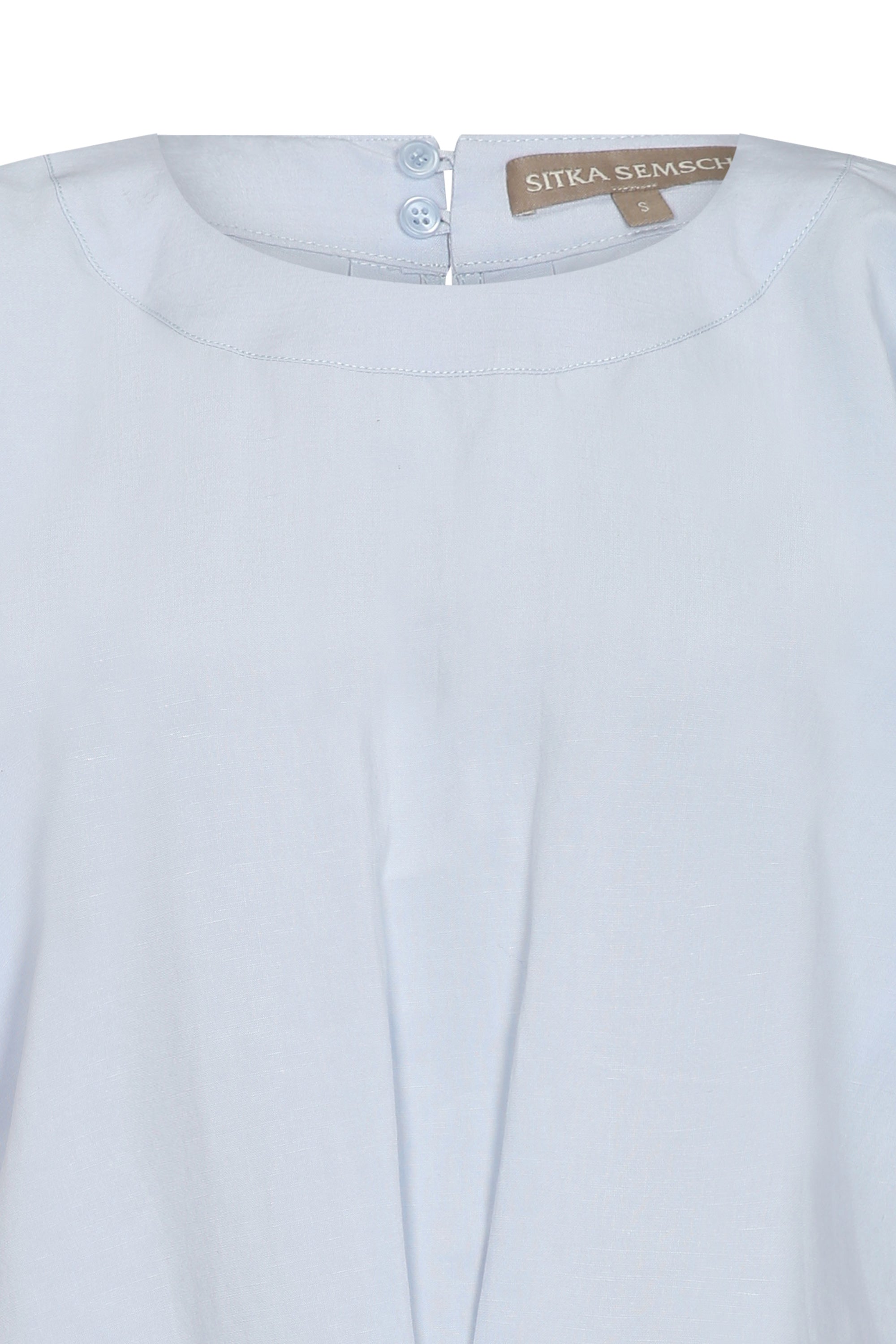 Shelby Blouse in Sky featuring a round neck, button-back detail, elasticated short sleeves, and tie hem for versatile styling.